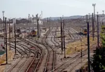 Hitachi Rail Chosen for ETCS Transition Module in Portugal A sprawling rail yard with multiple parallel and diverging tracks, overhead electric lines, and distant trains.