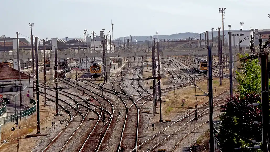 A sprawling rail yard with multiple parallel and diverging tracks, overhead electric lines, and distant trains.