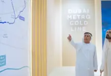 UAE Approves $9.3 Billion Metro Gold Line Project in Dubai Two men in traditional Emirati dress stand beside a Dubai Metro Gold Line exhibit, one pointing at a large map showing the route.