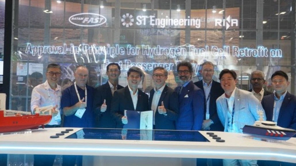 Group of professionals at a conference posing for a photo in front of a banner about hydrogen fuel cell retrofit, with models on the display table and company logos overhead.