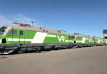 Siemens Completes VR’s Vectron Electric Locomotive Order Row of modern VR locomotives in green and white livery parked outside a train maintenance yard under a clear blue sky, extending into the distance