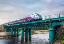 Ireland Taps Stadler to Modernize Railway with FLIRT Trains High-speed train crossing a teal metal bridge over a shallow river at sunset.