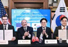 MASGA Project Advances S Korea-U.S. Shipbuilding Cooperation Four men in suits sit at a table signing documents during a memorandum of understanding ceremony, with U.S. and South Korean flags in the background.