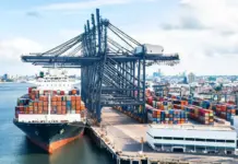 APM Terminals to Boost Nigerian Ports with $600M Investment Container ship at a busy port with stacked cargo containers and a large gantry crane overhead.