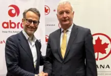 Air Canada, Abra Boost Commercial Partnership in Americas Two men in business suits shake hands at a Canada-themed event backdrop with red logos and banners behind them.