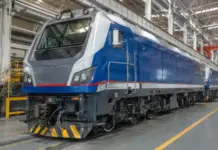 Azerbaijan Taps China for Railway Locomotive Fleet Expansion Blue and gray locomotive in a maintenance shop, front view, with yellow safety rails nearby and overhead cranes.
