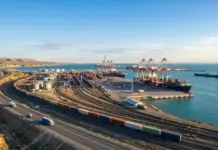 Kazakhstan Invites Cyprus to Join Middle Corridor Upgrade Port with container cranes, stacked shipping containers, and parallel rail tracks along the coast.