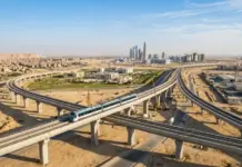 Chinese Concessional Loan to Boost Egypt’s Cairo Light Rail Elevated blue train traveling on a curved viaduct above a sandy desert cityscape with tall skyscrapers in the distance.