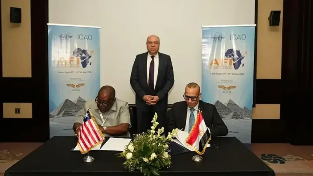 Two men sit at a table signing documents; flags of the United States and Egypt on the table, with a man standing behind them and ICAO banners in the background.
