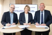 Safran and Lufthansa Technik Ink Long Term Support Agreement Three business professionals sign documents at a round conference table during a formal signing ceremony, with a screen in the background.