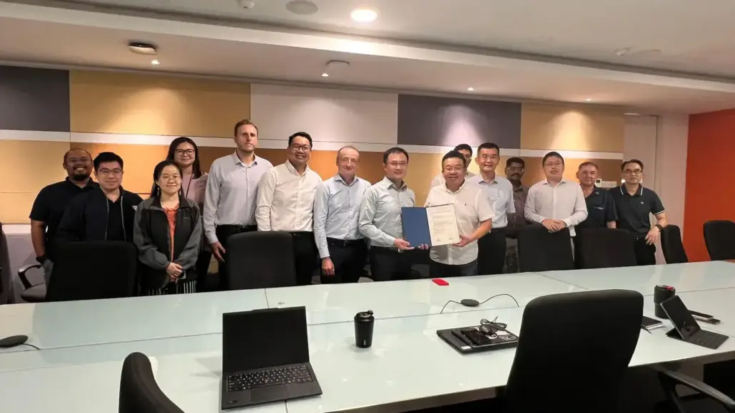 Group of professionals posing in a conference room, one person in front holding a certificate folder prominent in the center